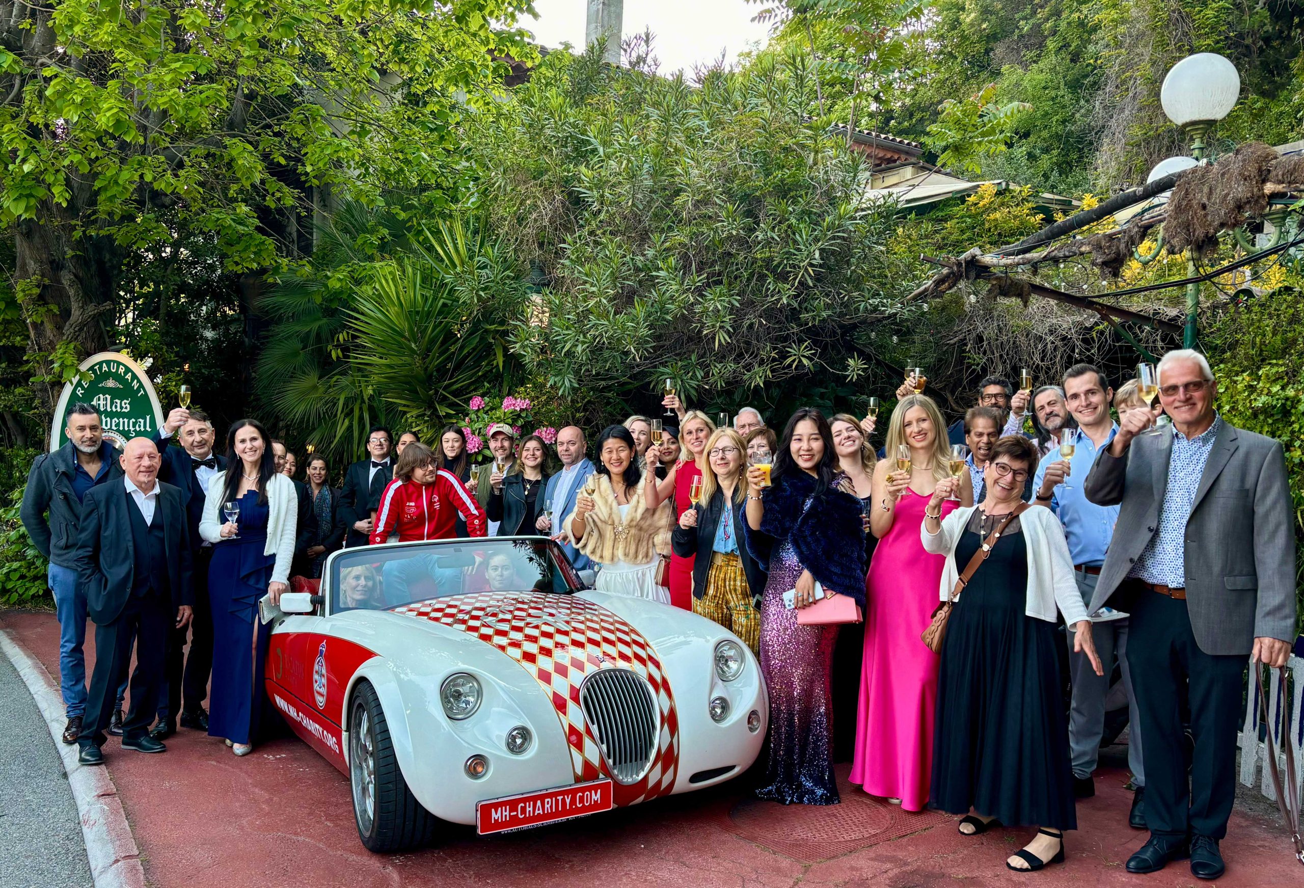 Gäste in Abendgarderobe stoßen rund um den MH-Charity Roadster an, im Hintergrund ein Garten.