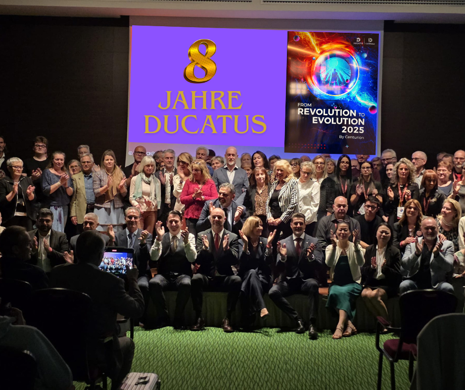 Großes Gruppenfoto auf der Bühne, im Hintergrund steht „8 Jahre DUCATUS“, viele Teilnehmer applaudieren