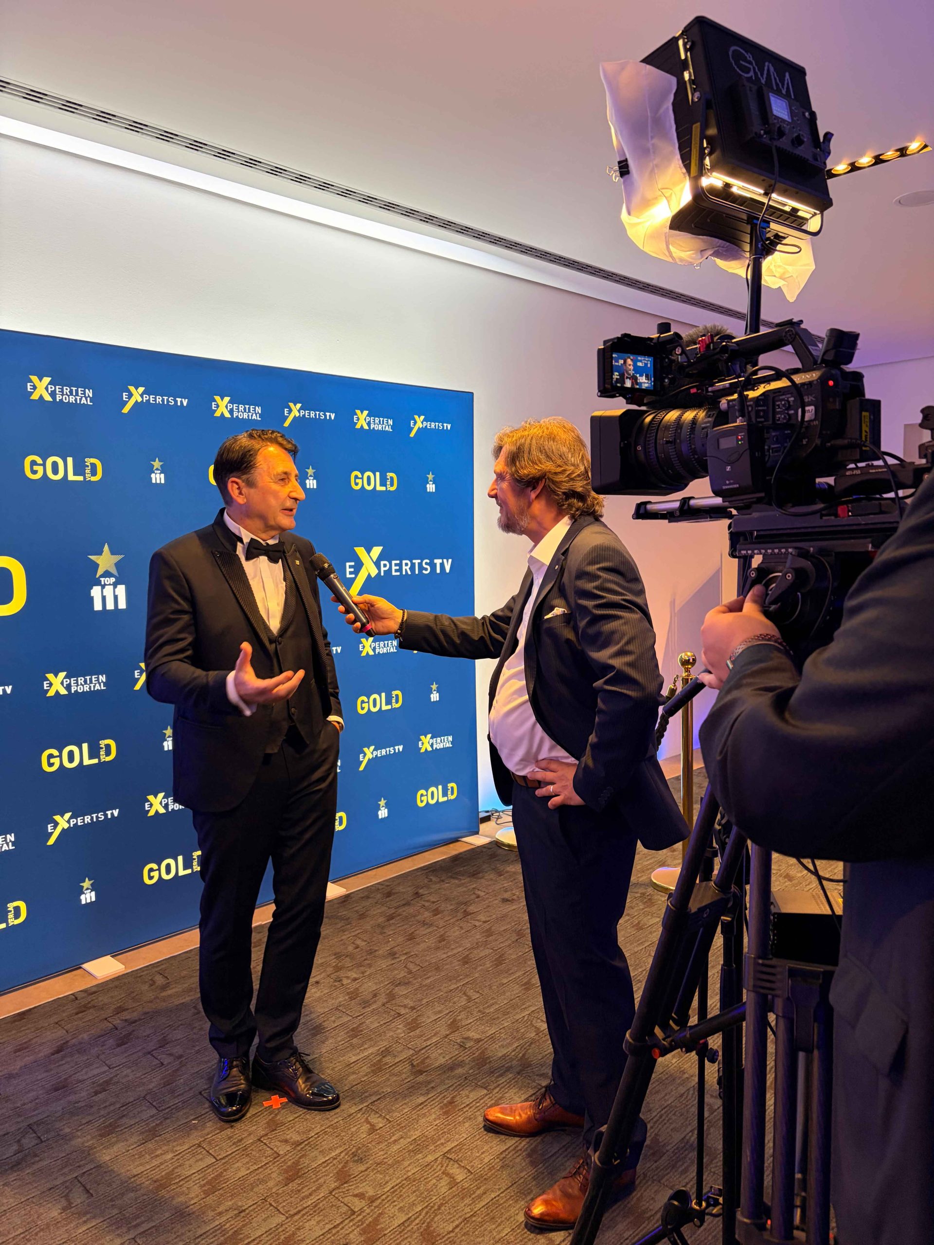 Mario Hintermayer nimmt die Auszeichnung „Top 111 Public Speakers 2025“ entgegen und steht neben einem Mann im Smoking, rechts ein großes „Top 111 Public Speakers 2025“-Banner.