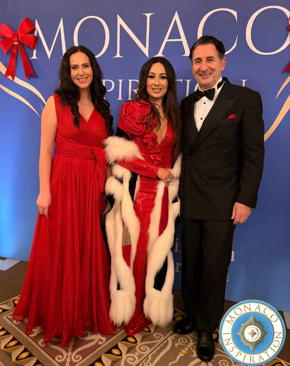 Drei Personen posieren vor einer „Monaco Inspirations Club“ Fotowand, alle tragen festliche Kleidung.